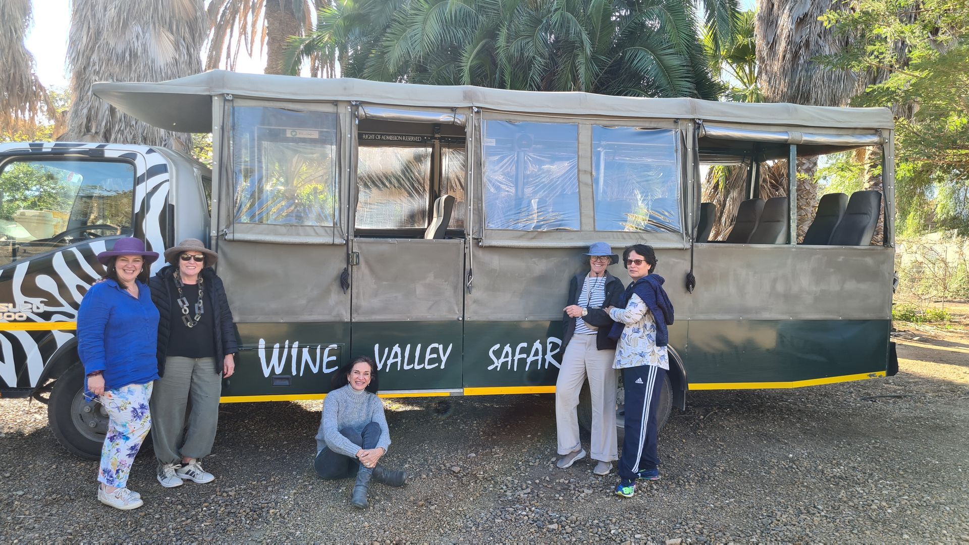 Group of women pose in front of safari vehicle, 