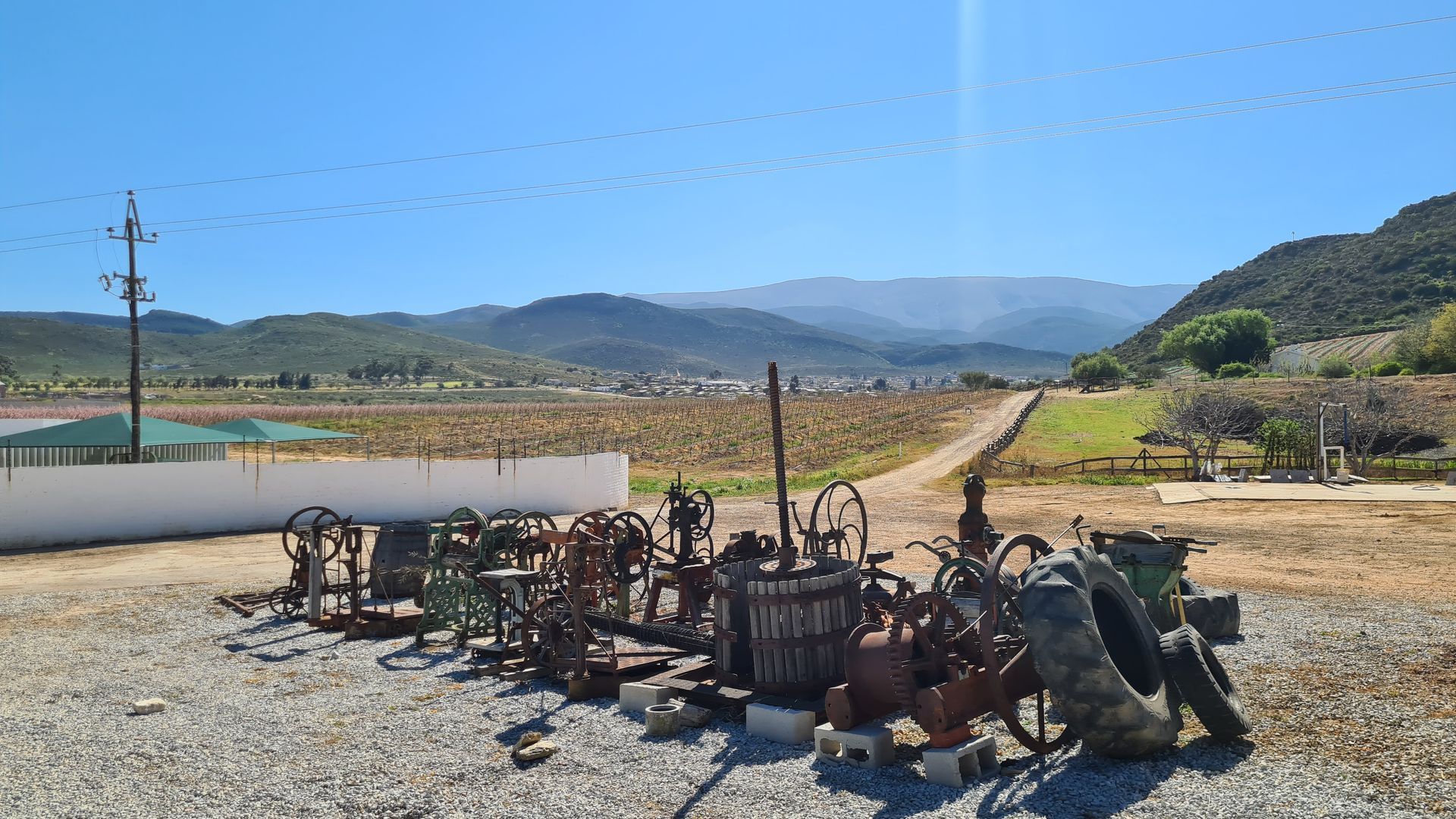 A collection of old farm equipment, with a vineyard and mountain backdrop under a blue sky.