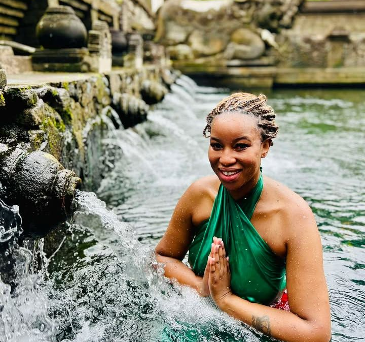 Woman in green wrap, in water, hands together. Water flows from stone fountain in background.