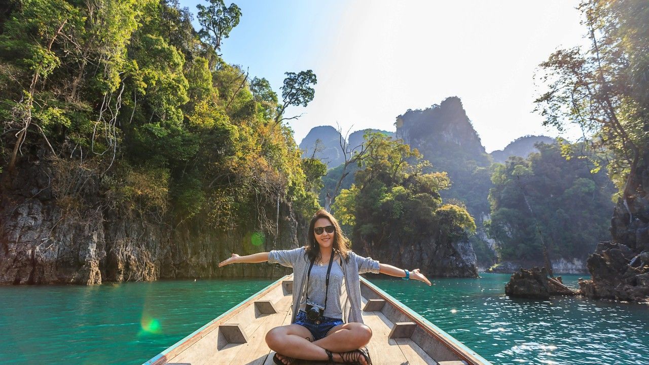 Woman on a boat with arms outstretched, smiles, surrounded by limestone cliffs and turquoise water.