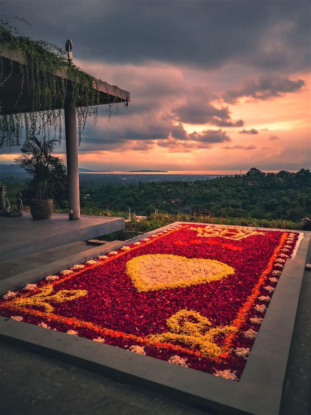 Floral arrangement in heart shape on red rug, overlooking landscape at sunset.