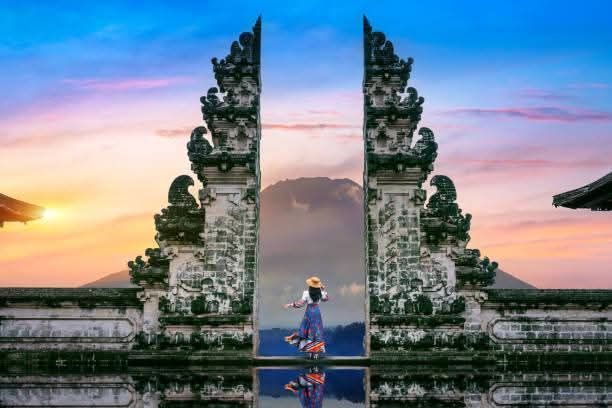 Woman standing in gateway, Mount Agung visible, sunset colors in Bali.