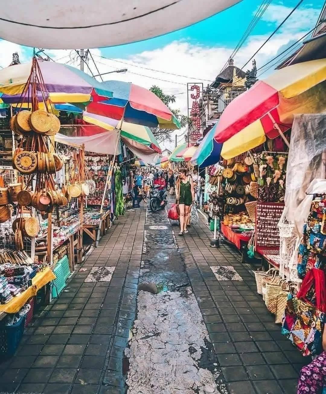 A vibrant outdoor market with colorful umbrellas. People browse stalls filled with crafts and souvenirs.