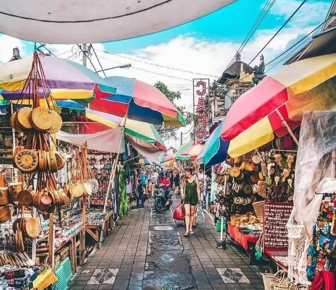 Busy Bali market scene with colorful umbrellas, shops, and people walking.