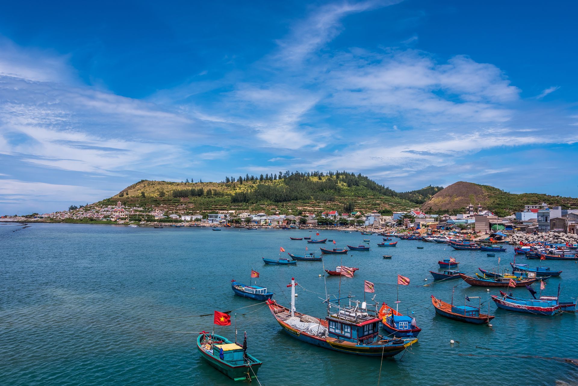 Boats on a bay near a coastal town, under a blue sky with hills in the background.