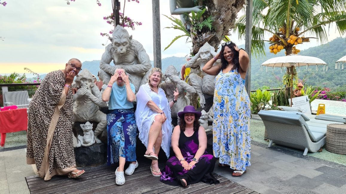 Group posing outdoors beside a statue, with one person in a leopard coat and another in a blue floral dress.