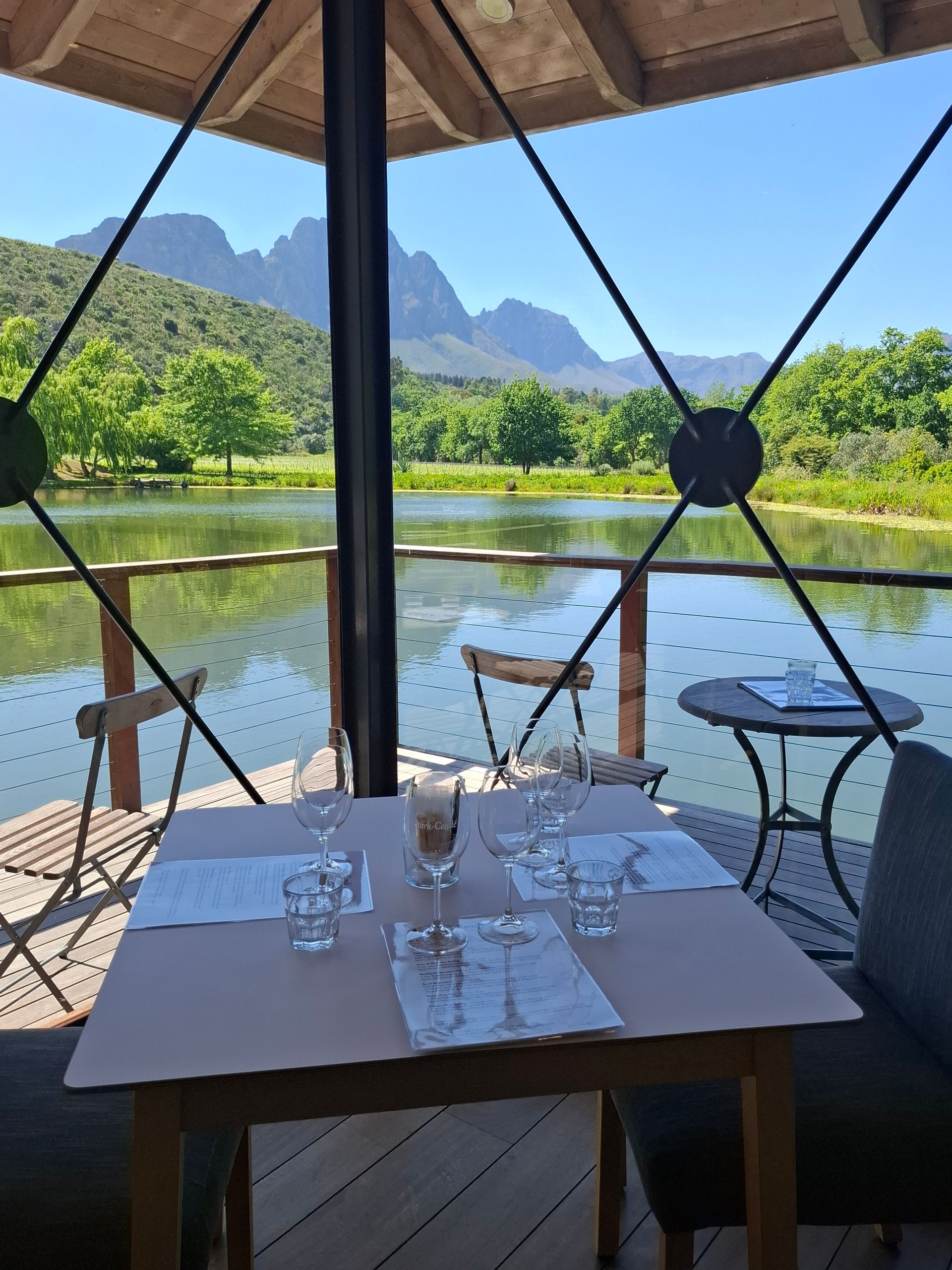 Table set for a meal on a deck overlooking a lake, with mountains in the background.