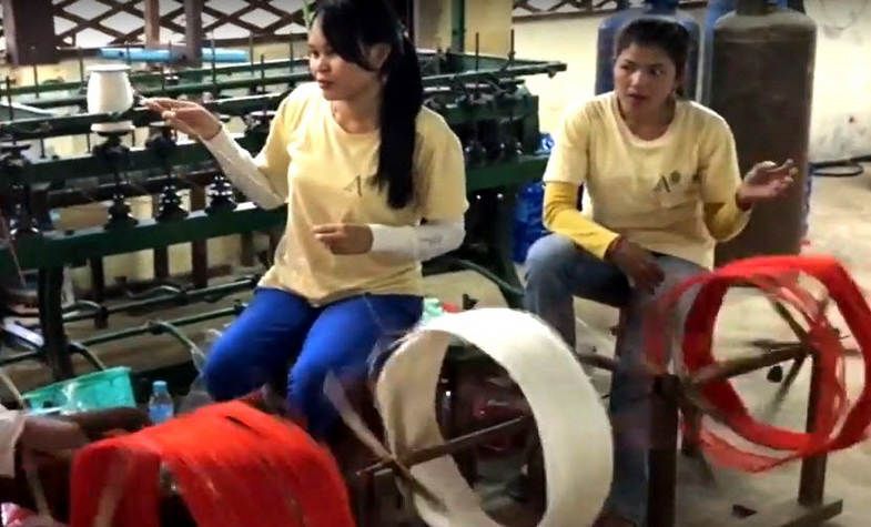 Two women working with colorful spools of thread near machinery in a workshop.