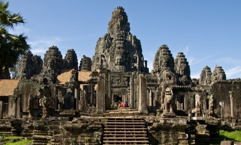 Ancient temple complex, Angkor Wat, Cambodia, stone structure with stairs, towers, and statues under blue sky.