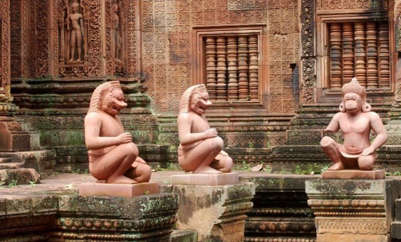 Three statues of monkeys in a temple, red stone, serene expressions, outdoor setting.