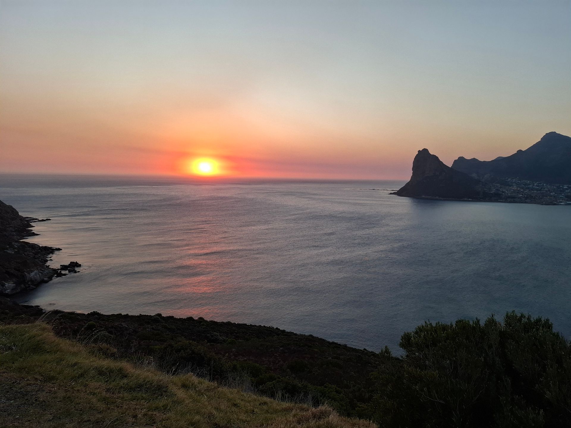 Sunset over ocean with silhouetted land on either side.