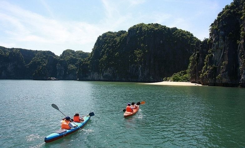Kayakers on blue water near lush, green limestone cliffs.