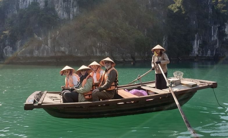 People in conical hats on a small boat in turquoise water near rock formations.