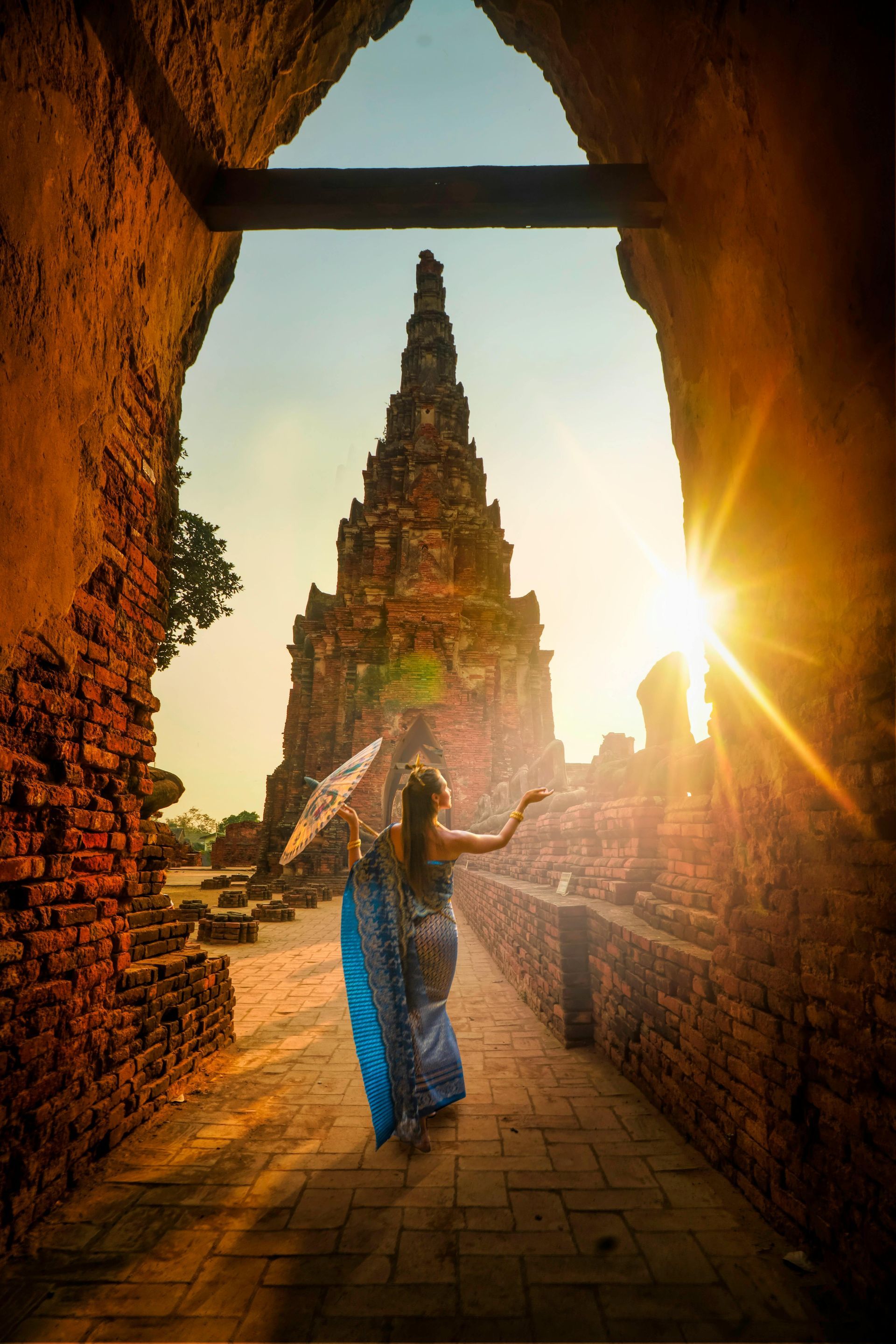 Woman in blue dress with umbrella at ancient temple ruins at sunset.