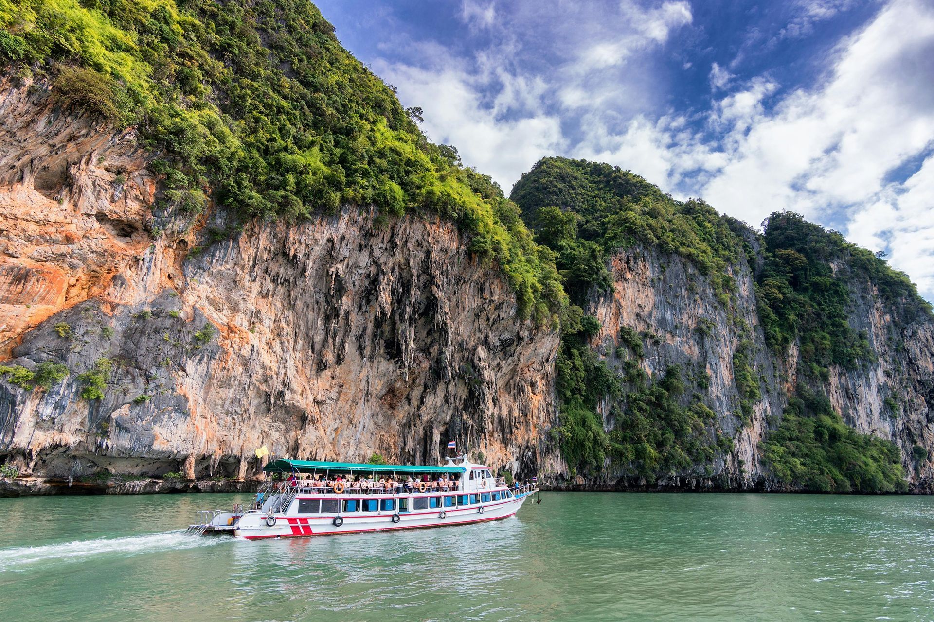 Boat on turquoise water near rocky cliffs covered in green vegetation under blue sky.