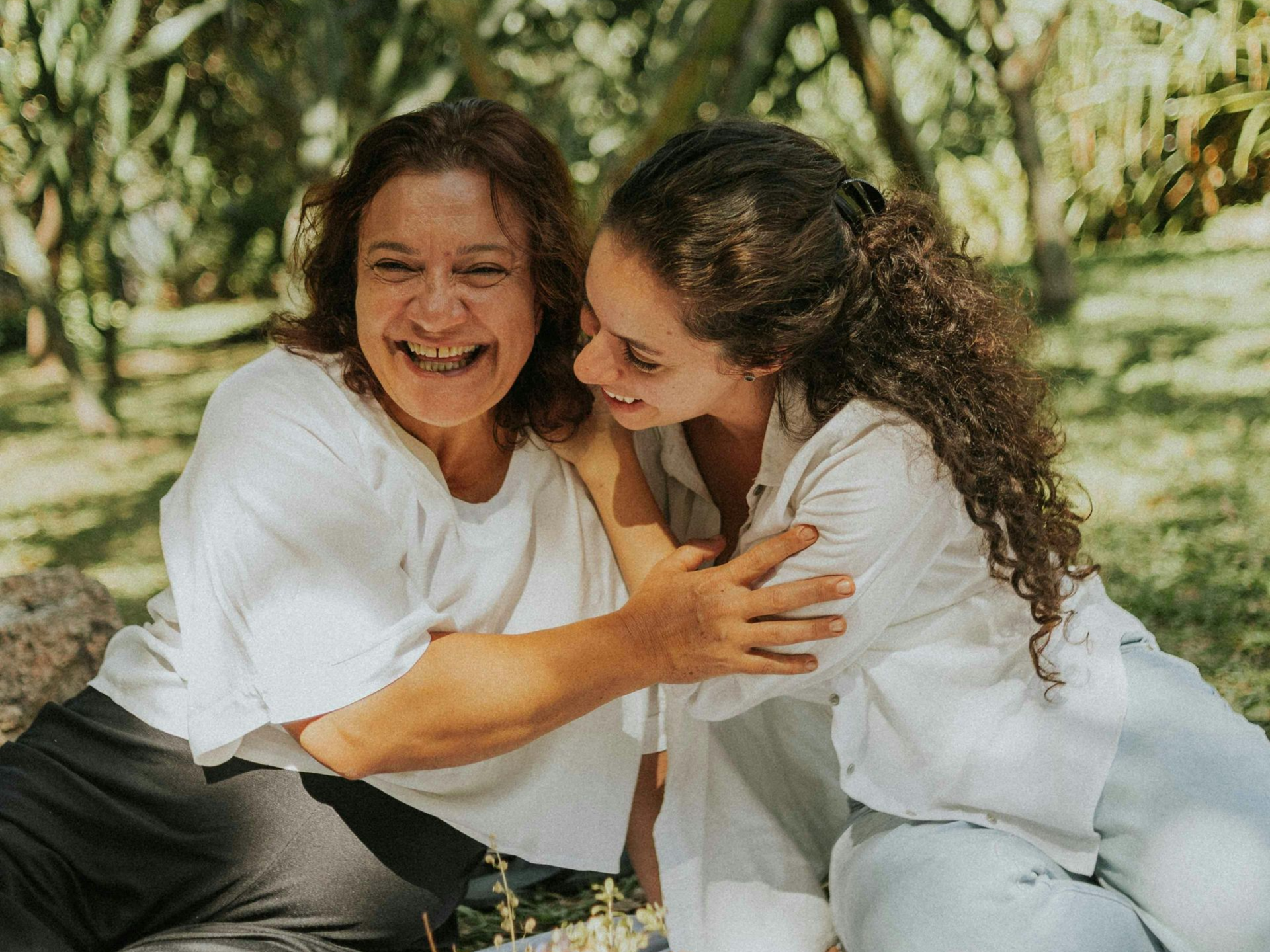 Three people stand on a gravel path outdoors by a rocky hillside, with one holding a bottle and gesturing to another.