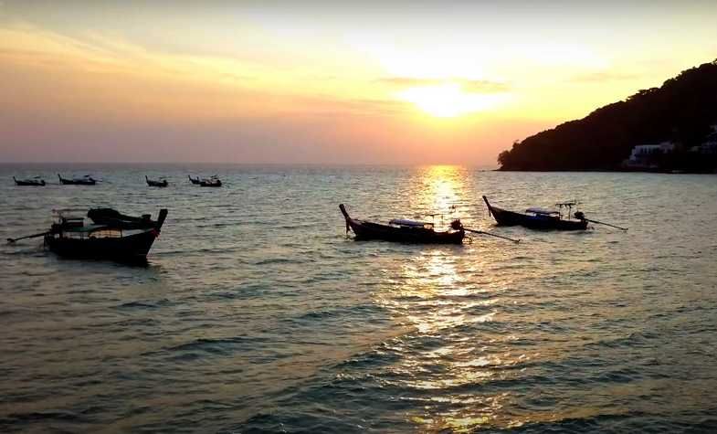 Boats on calm water at sunset, with a silhouette of a hill.