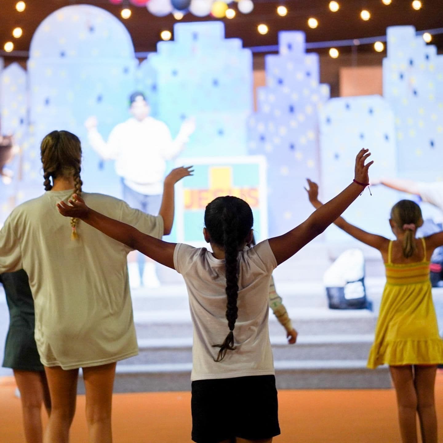 A group of young girls are standing in front of a large screen with their arms outstretched