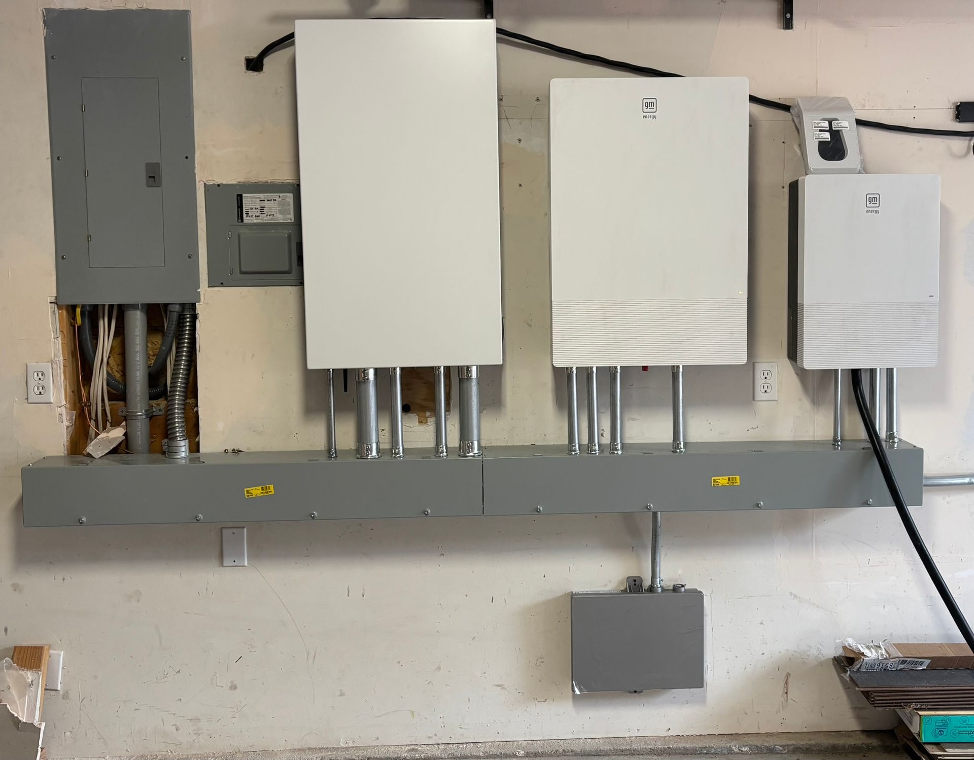 Electrical equipment installed on a garage wall; includes panels, conduit, and a gray support bar.