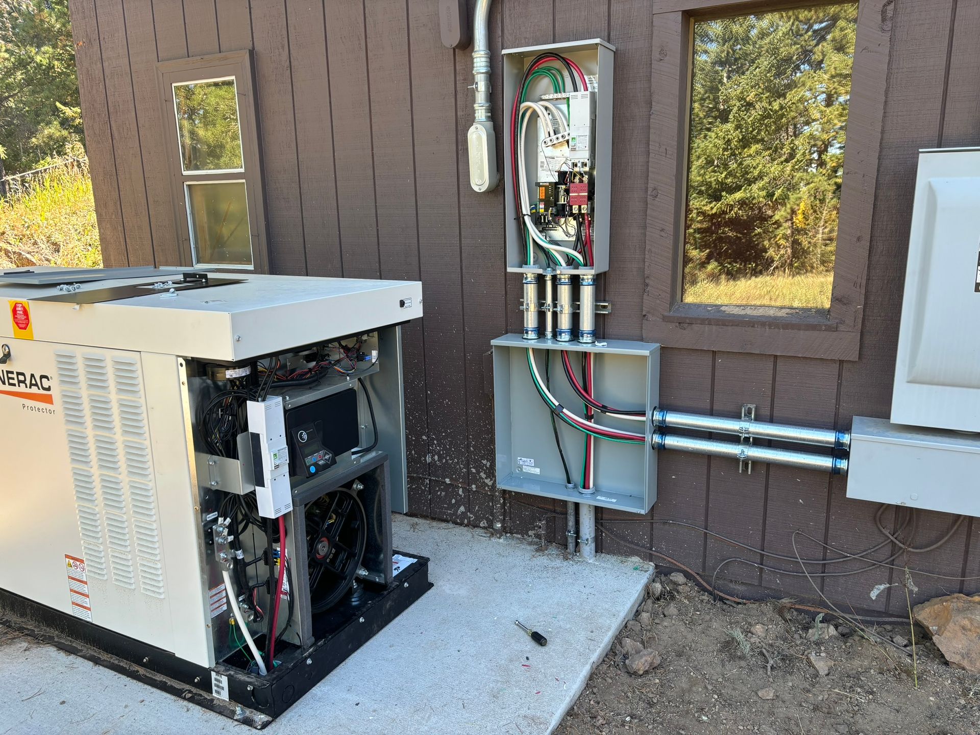 Generator and electrical box installed outdoors on a house; wiring visible.