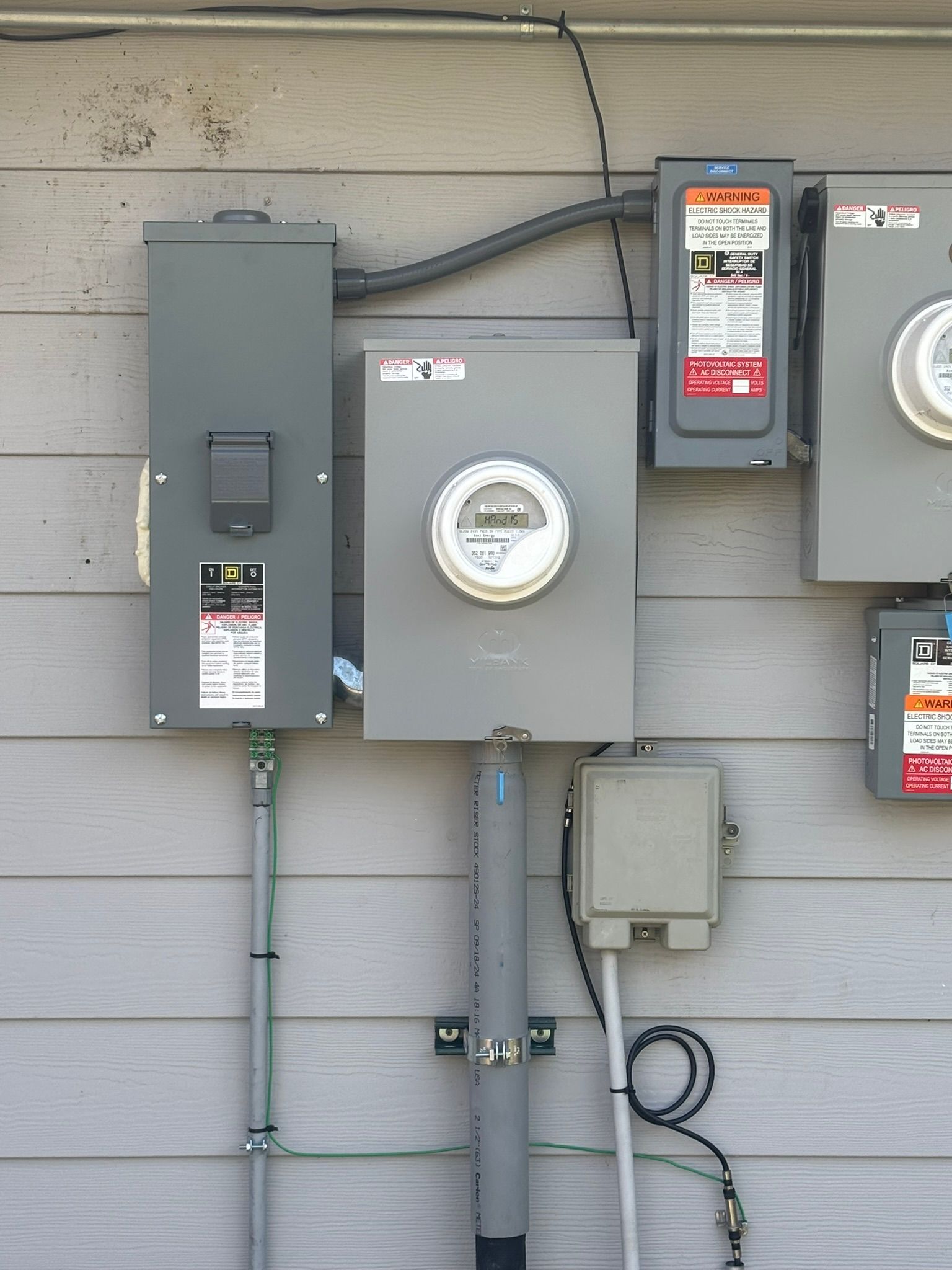 Electrical panel and meters mounted on a gray-sided exterior wall.