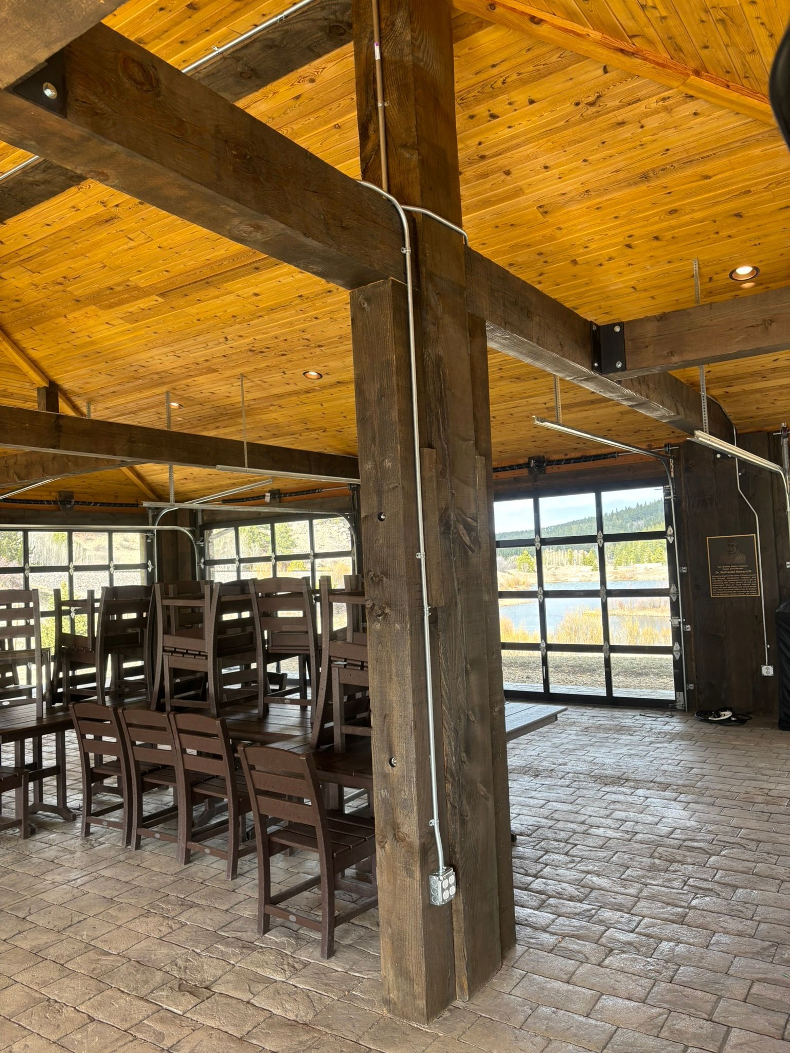 Wooden-beamed interior with chairs, glass doors, and a tiled floor. Electric wiring runs up the wooden support beam.