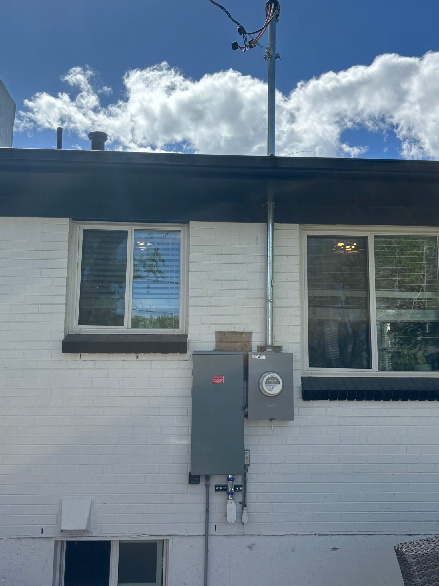 White brick building exterior with electrical panel, conduit, and antenna against a blue sky with clouds.