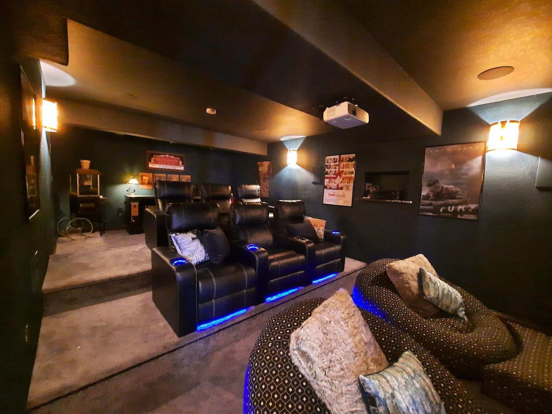 Home theater with black leather recliners, projector, and bean bag seating. Dark walls, low lighting.