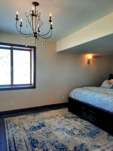 Bedroom with dark wood bed frame, rug, chandelier, and window.