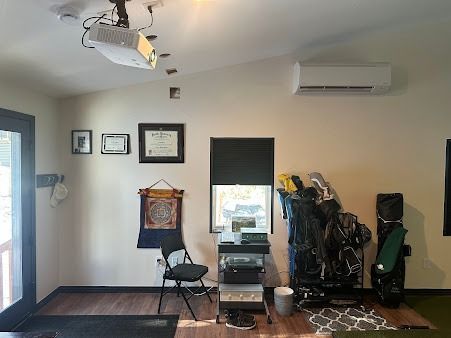 Indoor golf simulator room with golf bags, projector, and air conditioner.
