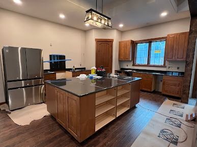 Kitchen under construction with island, cabinets, appliances, and brown wood floors.