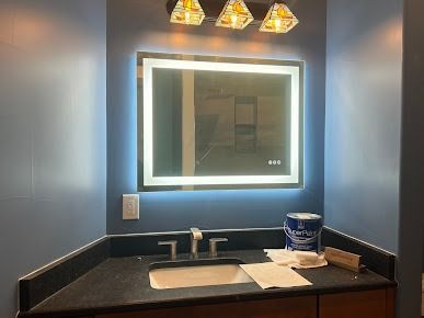 Bathroom with blue walls, black countertop, lit mirror, and sink.