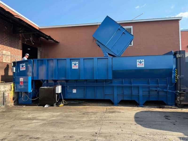 A large blue dumpster is parked in front of a building.