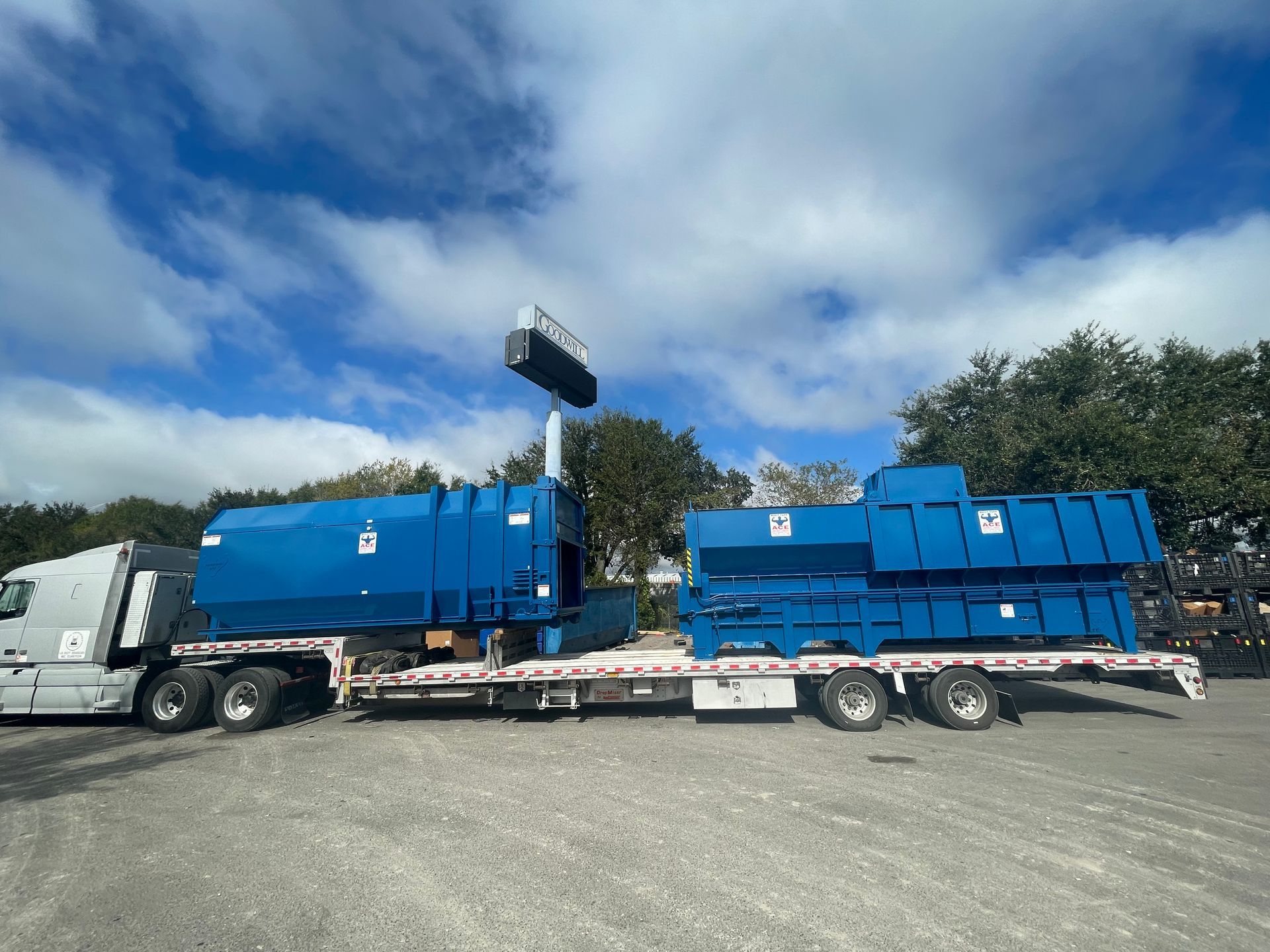 A truck is carrying two blue dumpsters on a trailer.