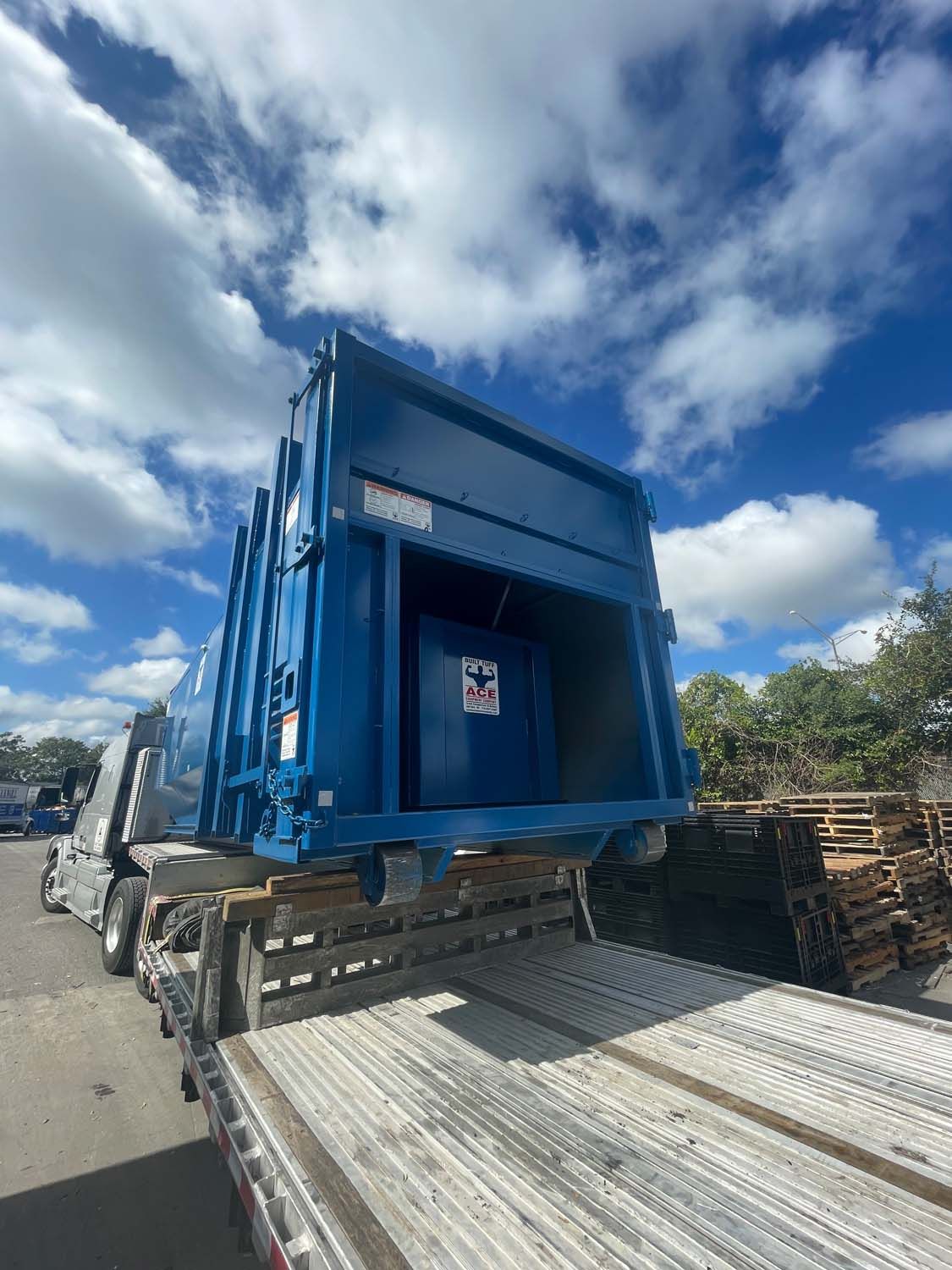 A blue dumpster is sitting on the back of a semi truck.