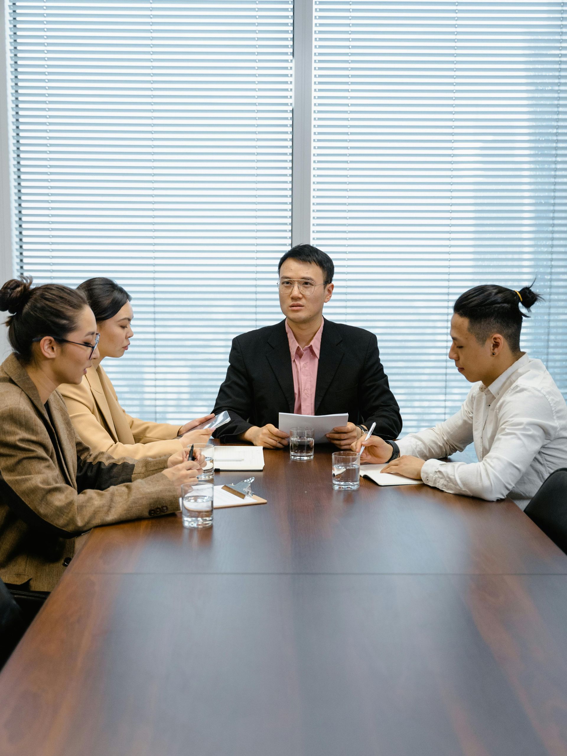 Four people sitting around a long wooden conference table in an office, reviewing documents
