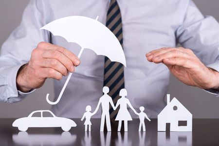 A man is holding an umbrella over a paper cut out of a family , car , and house.