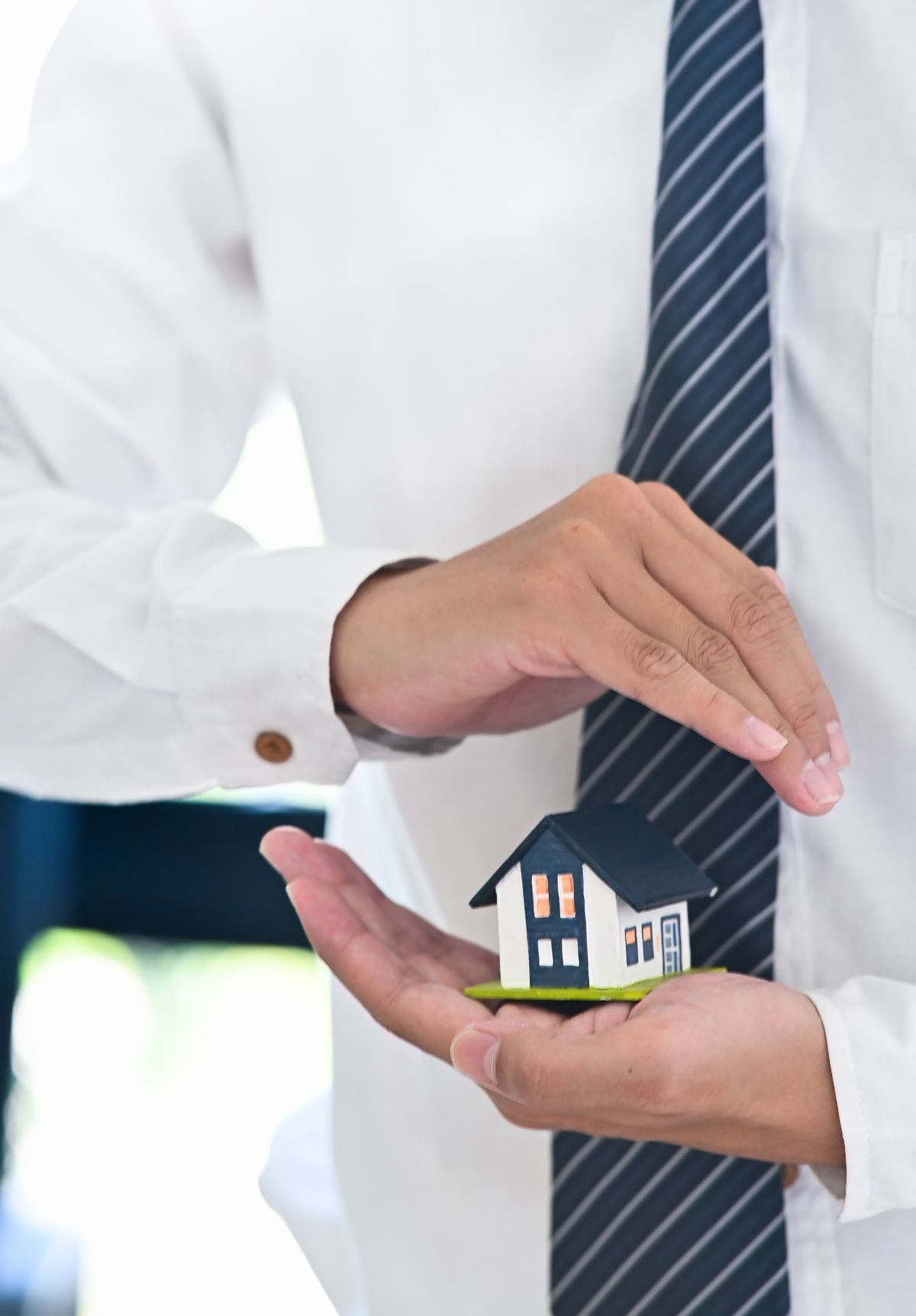 A man in a tie is holding a model house in his hands.