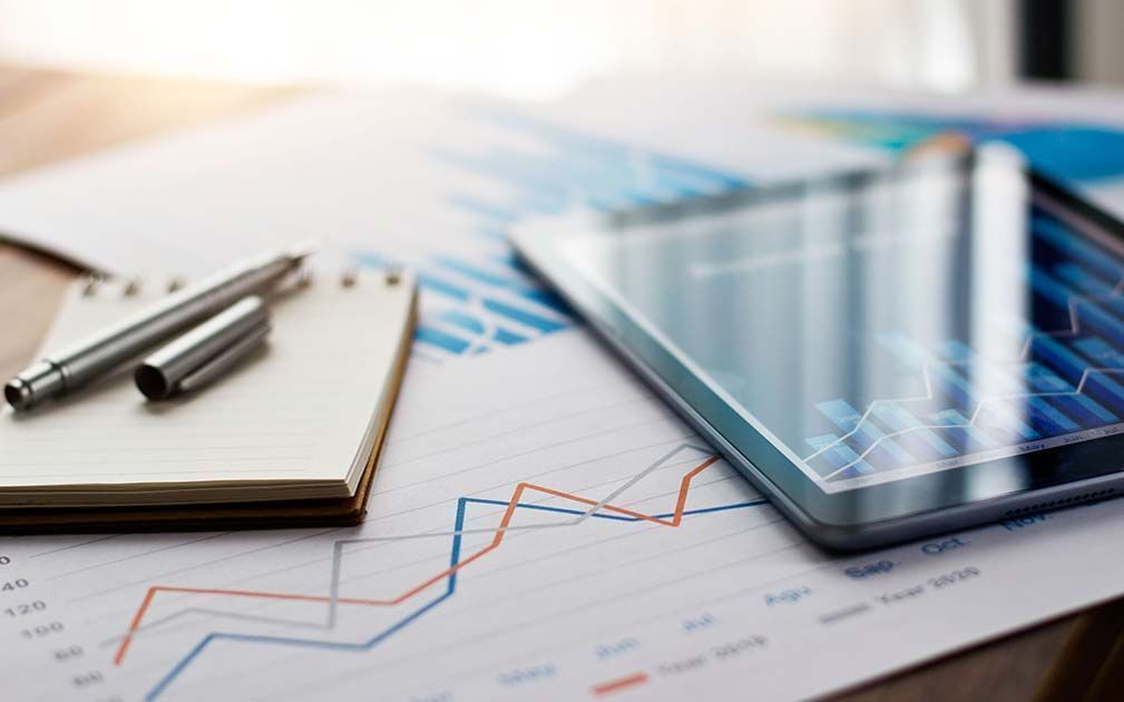 A tablet , a notebook , a pen , and a graph are on a table.