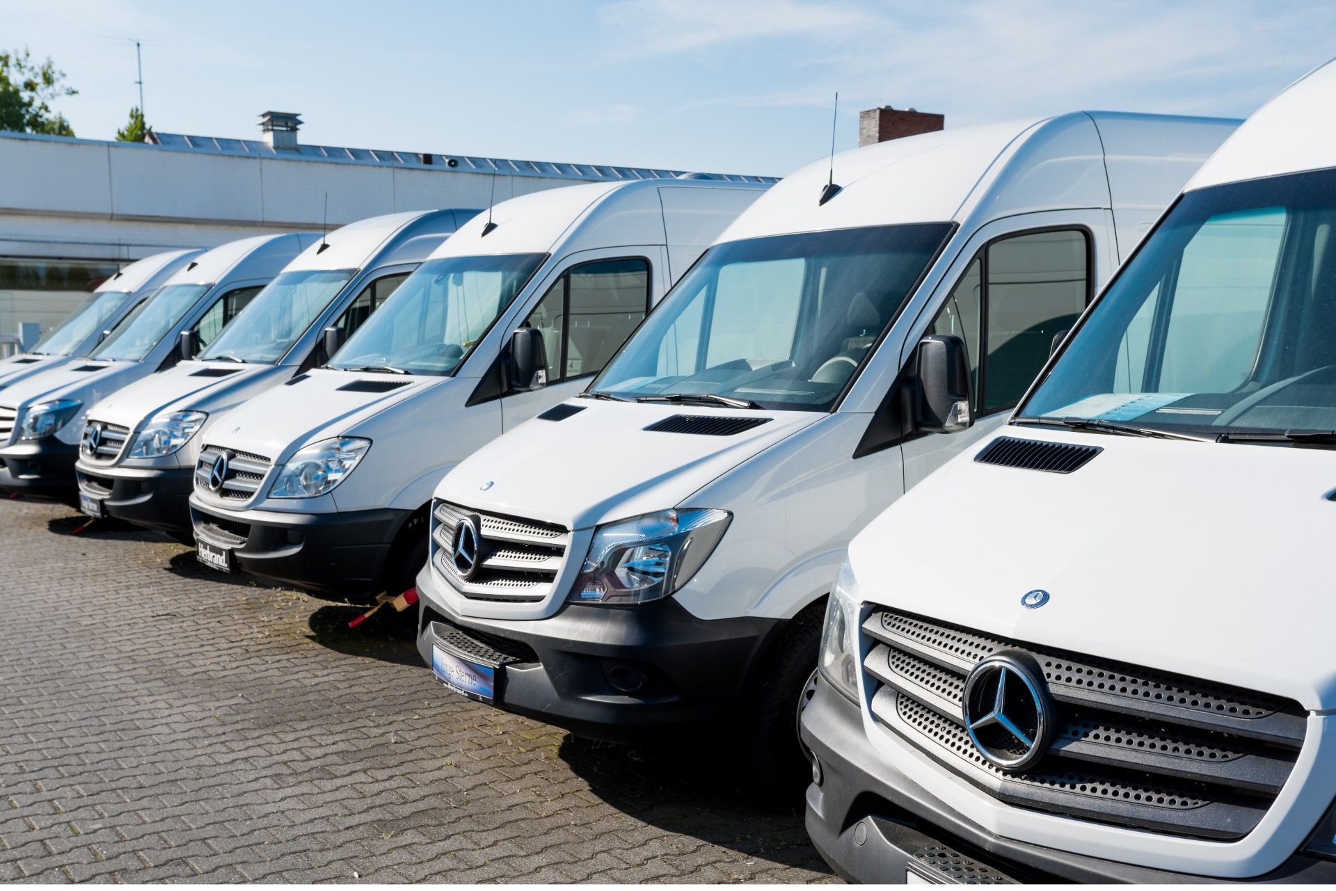 A row of white vans are parked in a parking lot.