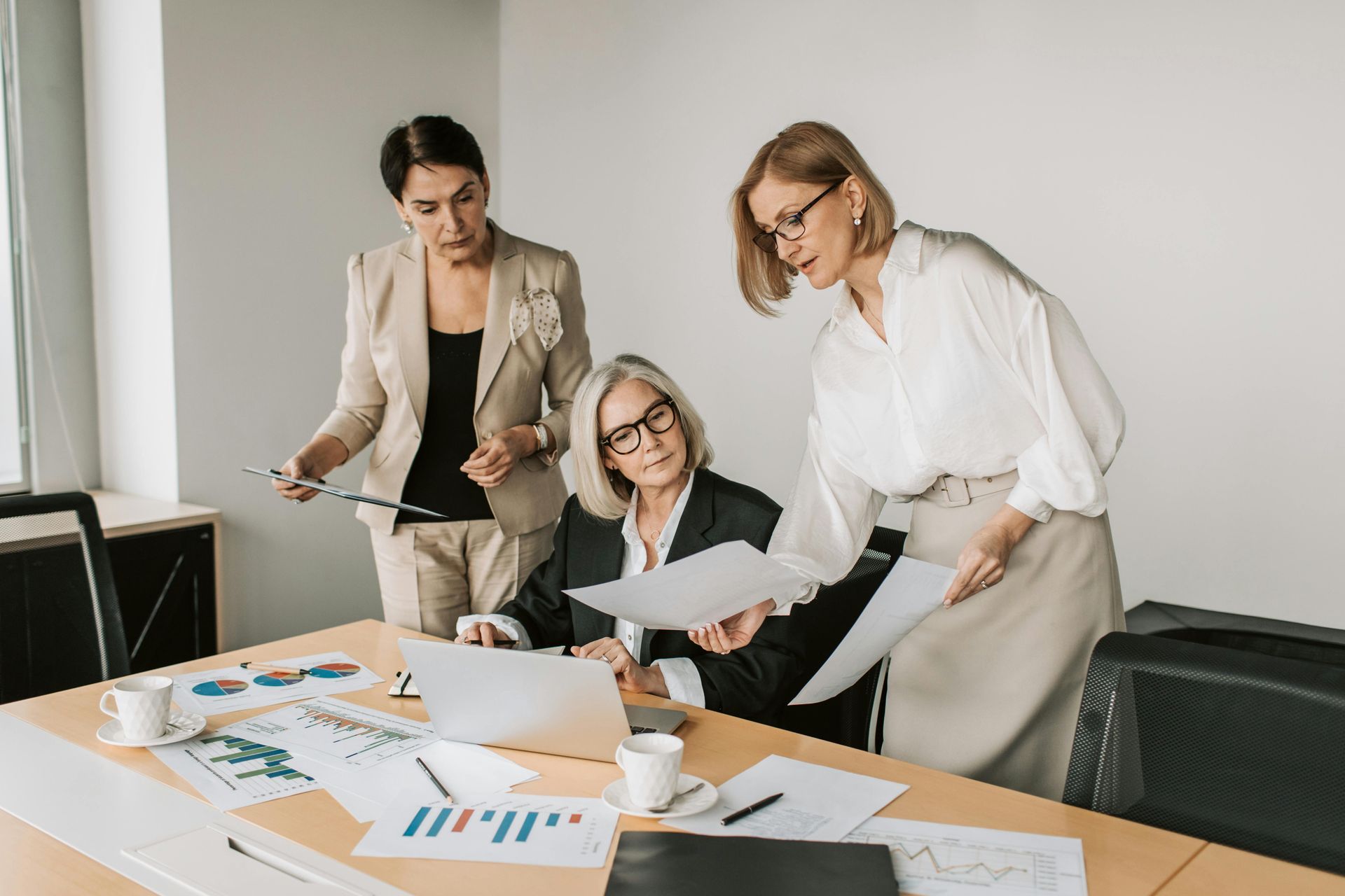 Three women are sitting at a table looking at papers and a laptop.