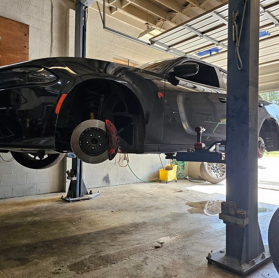 Black Vehicle Being Serviced on a Hydraulic Lift | Devoted Automotive