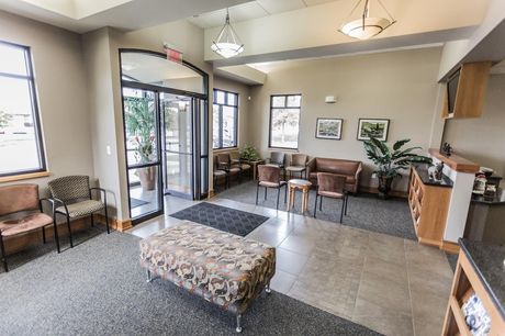 A waiting room with a bench , chairs , tables and a door.