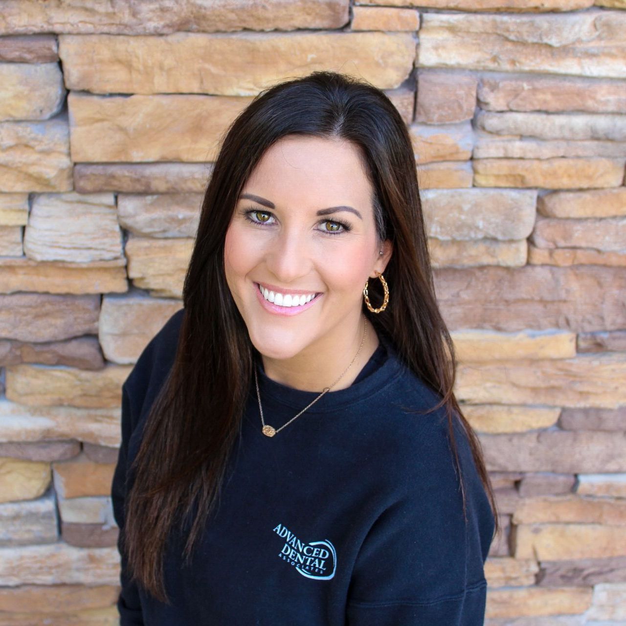 A woman is smiling in a circle in front of a brick wall.