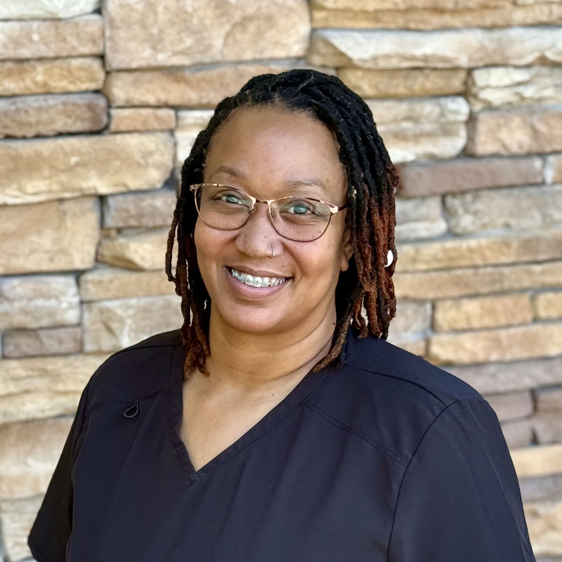 A woman is smiling in a circle in front of a brick wall.