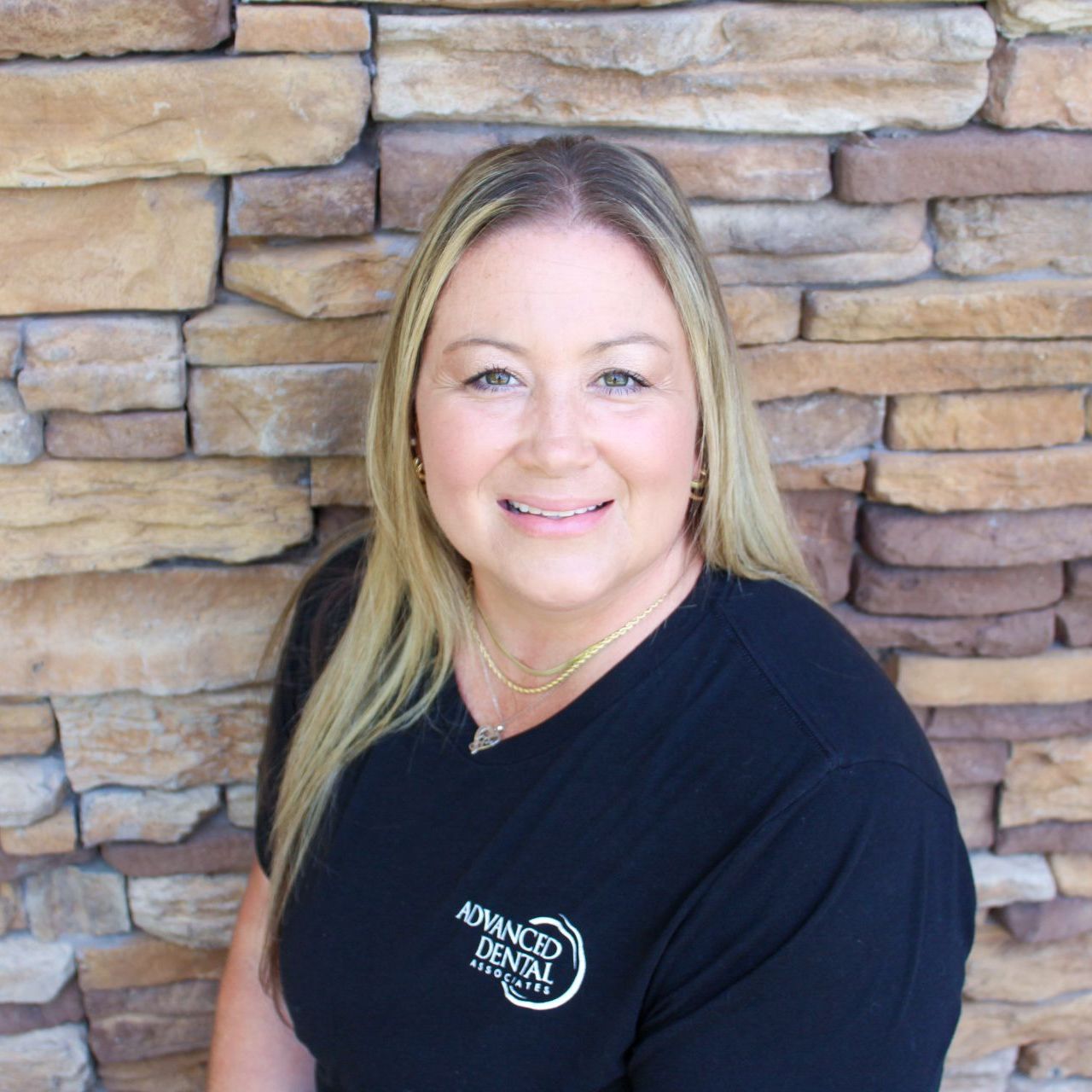 A woman in a black shirt is smiling in front of a stone wall.