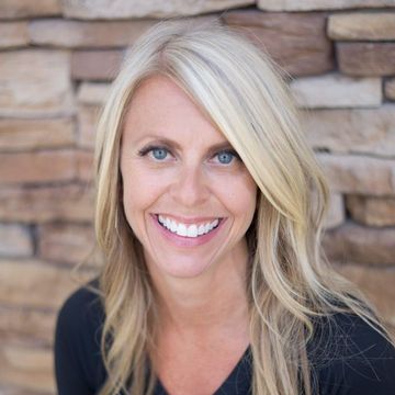 A woman is smiling in front of a stone wall.