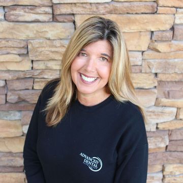 A woman is smiling in front of a brick wall.