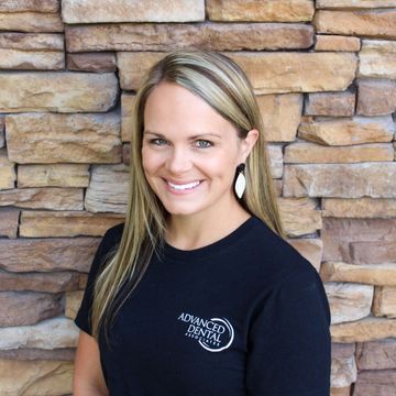 A woman with long blonde hair is smiling in front of a brick wall.