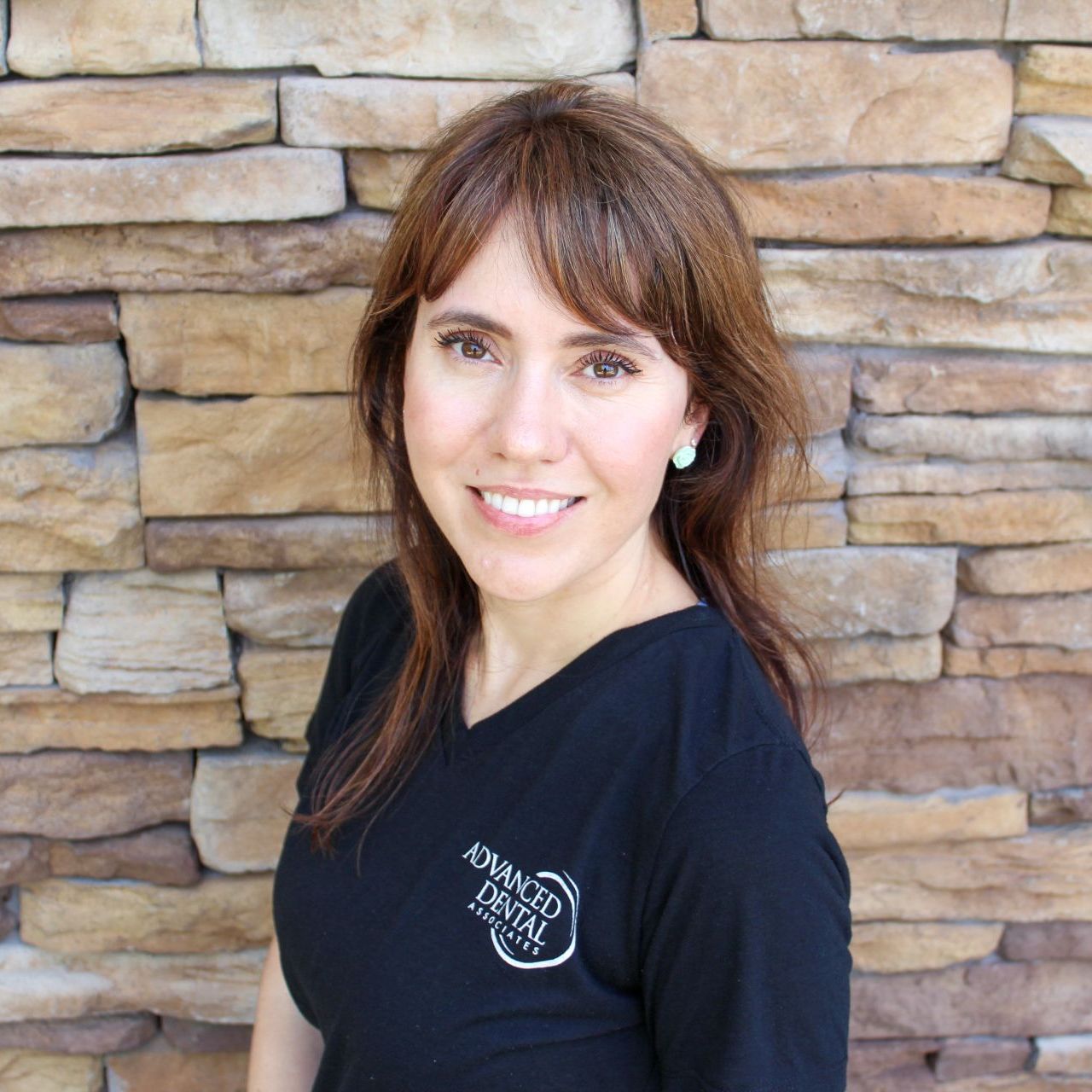 A woman wearing a stethoscope is smiling in front of a brick wall.